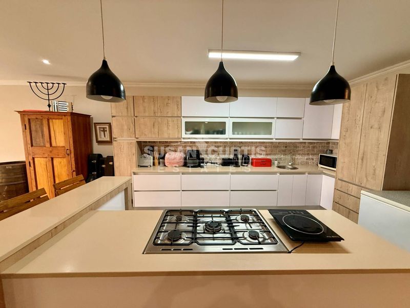 Modern kitchen featuring light wood and white cabinetry, stone countertops, a central gas hob, and stylish pendant lighting with a brick-style backsplash.