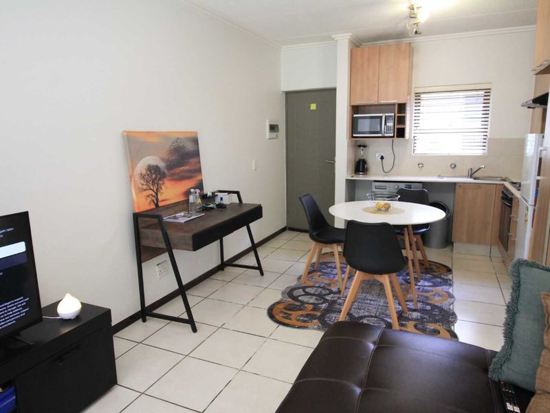 Open-plan living area featuring a compact kitchen with built-in cabinetry, oven, and tiled flooring throughout.