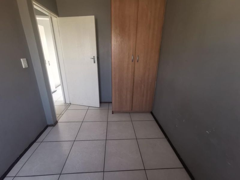 A simple bedroom featuring tiled flooring and a built-in wooden cupboard, offering a clean and functional space ready for personalization.