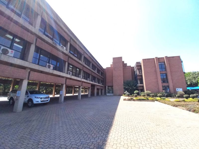 Exterior view of a multi-story brick office building featuring a covered parking area and paved driveway entrance.