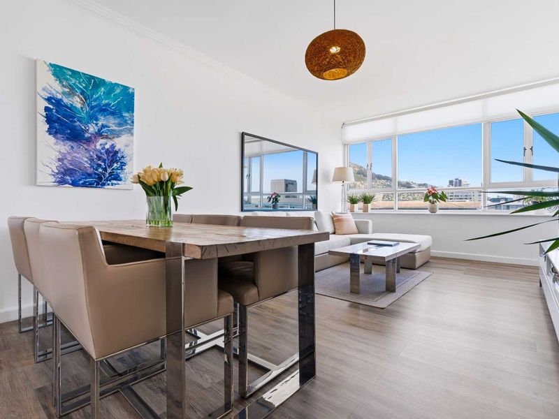 Bright open-plan living and dining area featuring large windows with city views, modern laminate flooring, and a clean, neutral aesthetic.