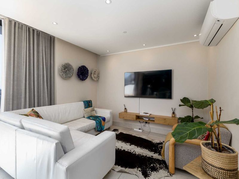A modern, well-lit living room featuring tiled floors, a wall-mounted air conditioning unit, and a floating media console with access to a balcony.