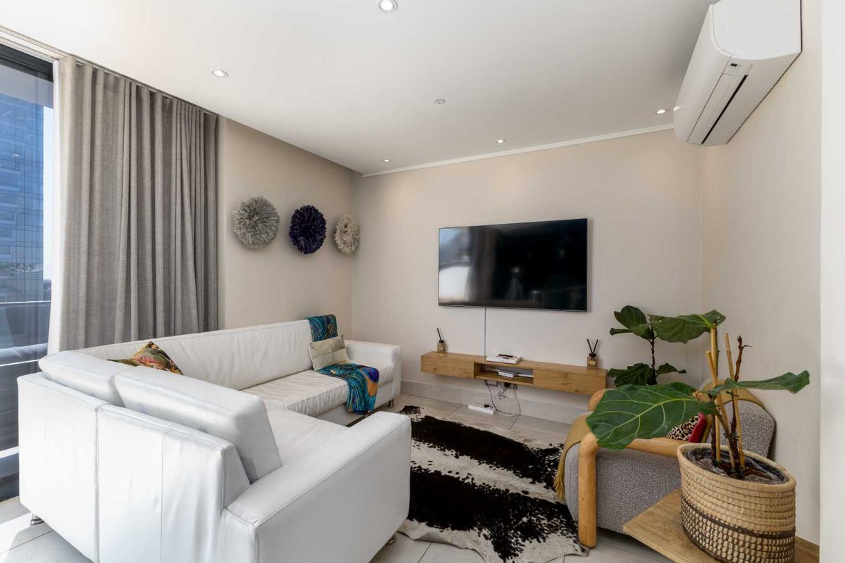 A modern, well-lit living room featuring tiled floors, a wall-mounted air conditioning unit, and a floating media console with access to a balcony.