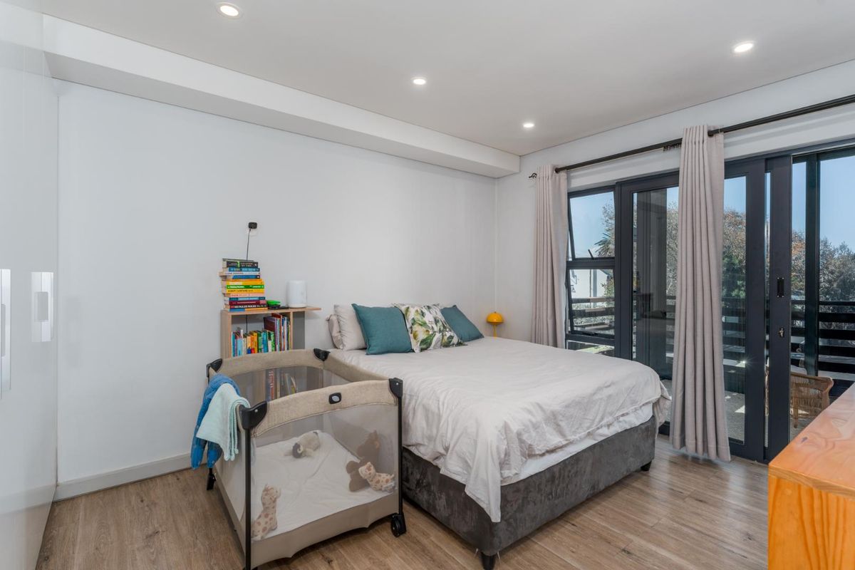 A bright bedroom featuring laminate flooring, recessed downlights, and a sliding glass door providing access to an outdoor balcony area.