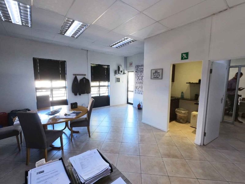 A functional office space featuring tiled flooring, suspended ceilings with integrated lighting, and an adjacent kitchenette area.