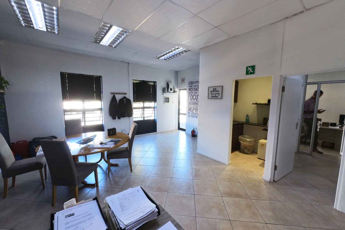 A functional office space featuring tiled flooring, suspended ceilings with integrated lighting, and an adjacent kitchenette area.
