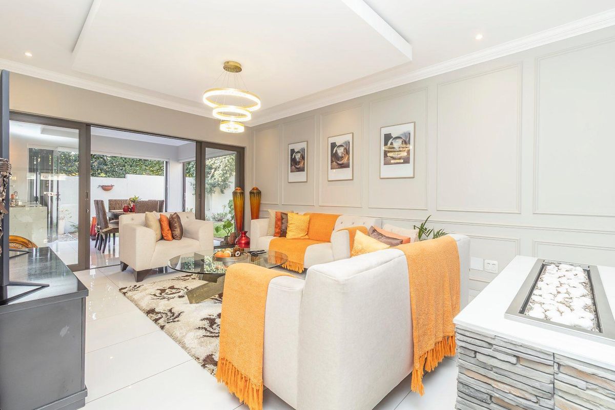 Spacious living room featuring elegant wainscoting, a recessed ceiling, stone-clad fireplace, and large sliding glass doors opening to an outdoor patio area.