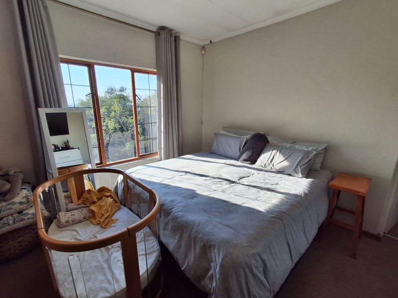 A well-lit bedroom featuring a large window with natural light, neutral wall finishes, and carpeted flooring.