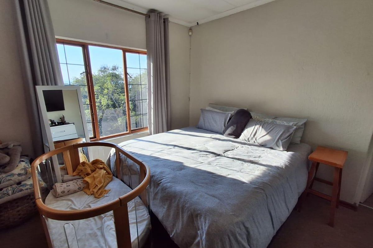 A well-lit bedroom featuring a large window with natural light, neutral wall finishes, and carpeted flooring.