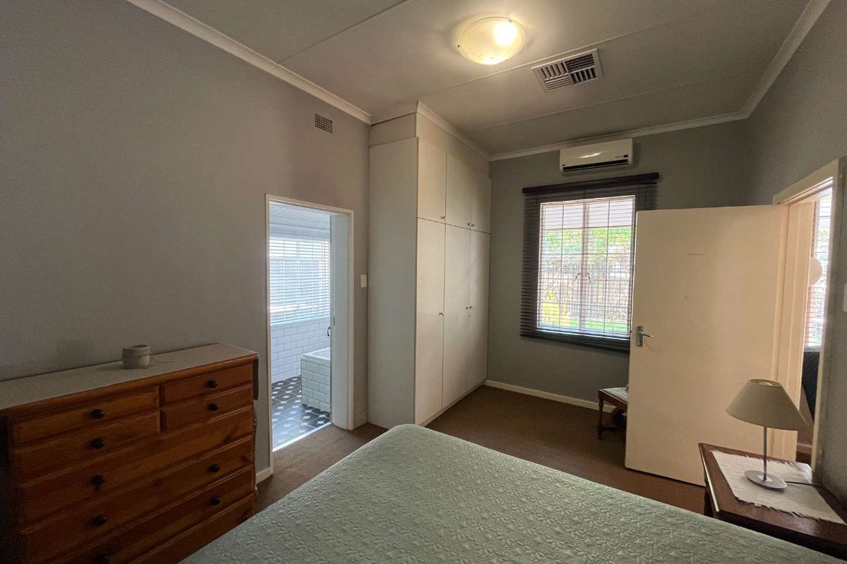 A functional bedroom featuring built-in cabinetry, a wall-mounted air conditioning unit, and direct access to an adjoining bathroom.