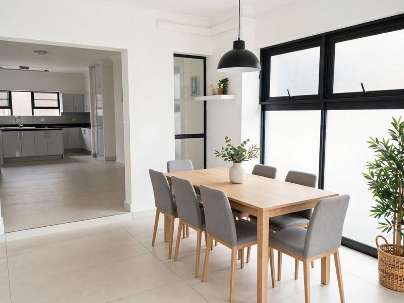 Bright open-plan dining area featuring modern tiled floors, large black-framed windows, and a seamless transition into a contemporary kitchen space.