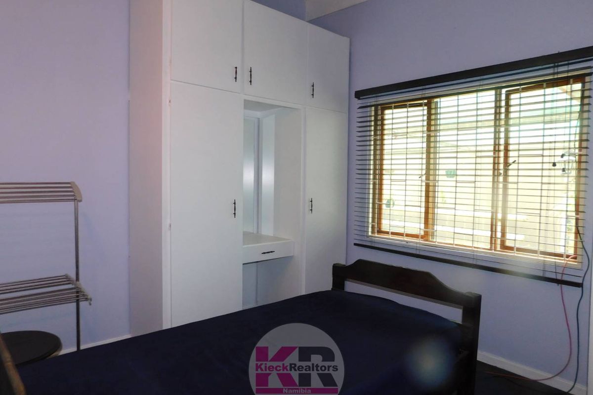 A bedroom featuring built-in white cabinetry with an integrated vanity desk and a window fitted with horizontal blinds.