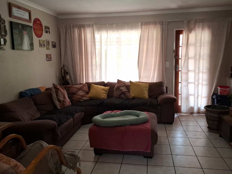 A comfortable living room featuring tiled flooring, a large window allowing natural light, and direct access to the exterior through a glass paneled door.