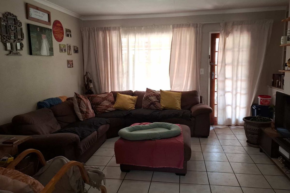 A comfortable living room featuring tiled flooring, a large window allowing natural light, and direct access to the exterior through a glass paneled door.