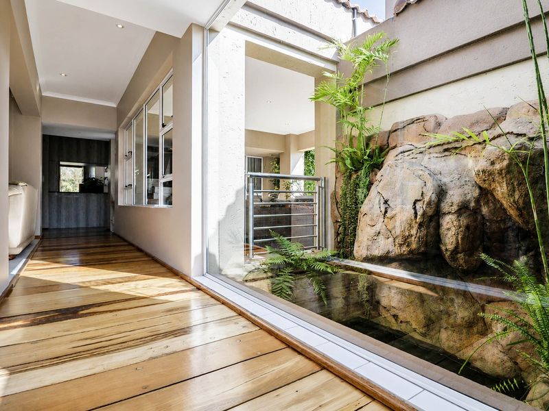 A bright, modern hallway featuring polished timber flooring, recessed lighting, and a unique indoor water feature with natural rock elements and glass partitioning.