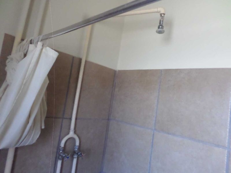 A basic bathroom shower area featuring exposed plumbing and neutral wall tiling, requiring modernization of fixtures.