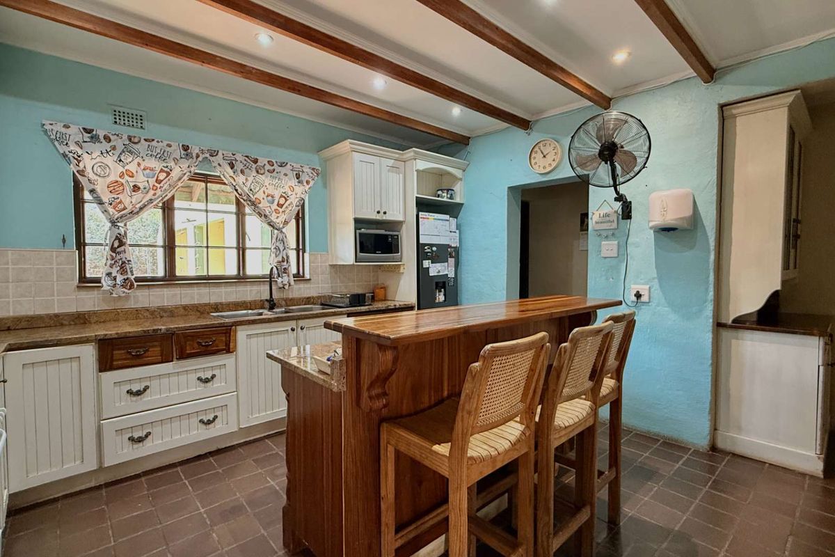 A rustic-style kitchen featuring exposed timber ceiling beams, granite countertops, built-in cabinetry, and a central breakfast bar with tiled flooring.