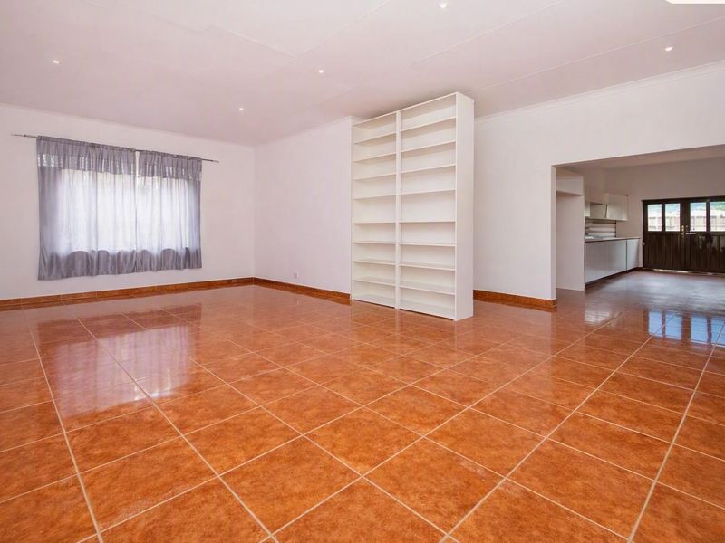 Spacious open-plan living area featuring polished terracotta-style floor tiles, built-in shelving, and recessed lighting, with a clear view into the adjacent kitchen space.