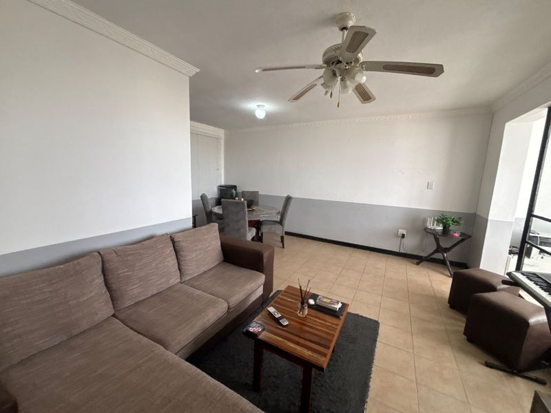 Open-plan living and dining area featuring tiled flooring, a ceiling fan, and crown molding, offering a functional space with potential for cosmetic updates.