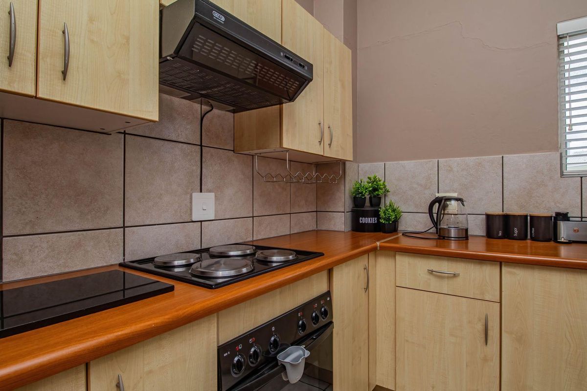 A functional kitchen featuring light wood cabinetry, a built-in oven with hob, extractor fan, and tiled splashbacks.