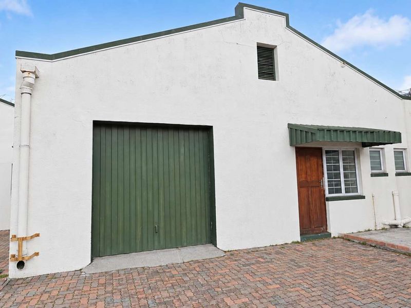 Front elevation of an office unit featuring a roller shutter door, paved driveway, and security fencing.