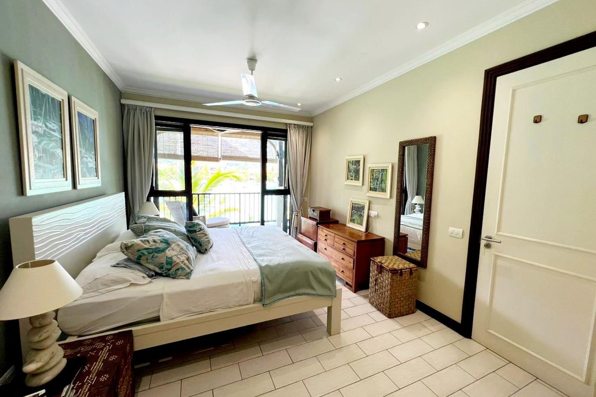 A well-maintained bedroom featuring tiled flooring, a ceiling fan, and direct access to a private balcony through sliding glass doors.