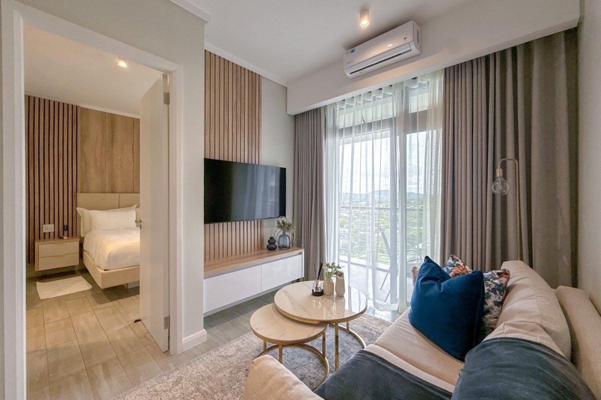 A modern living room featuring a timber slat feature wall, wall-mounted television, and split-system air conditioning, with an adjacent bedroom visible through the doorway.