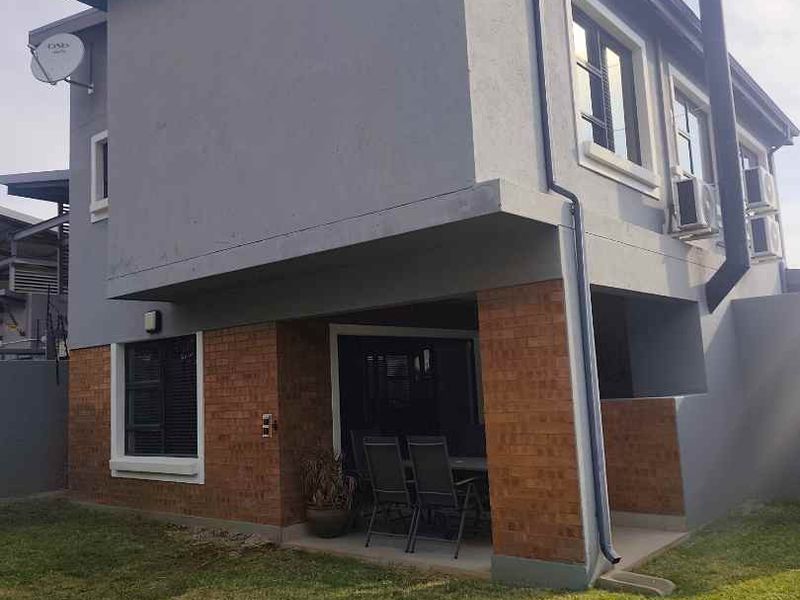 Rear view of a two-story house featuring a covered patio, brick and plaster exterior finishes, and external air conditioning units.