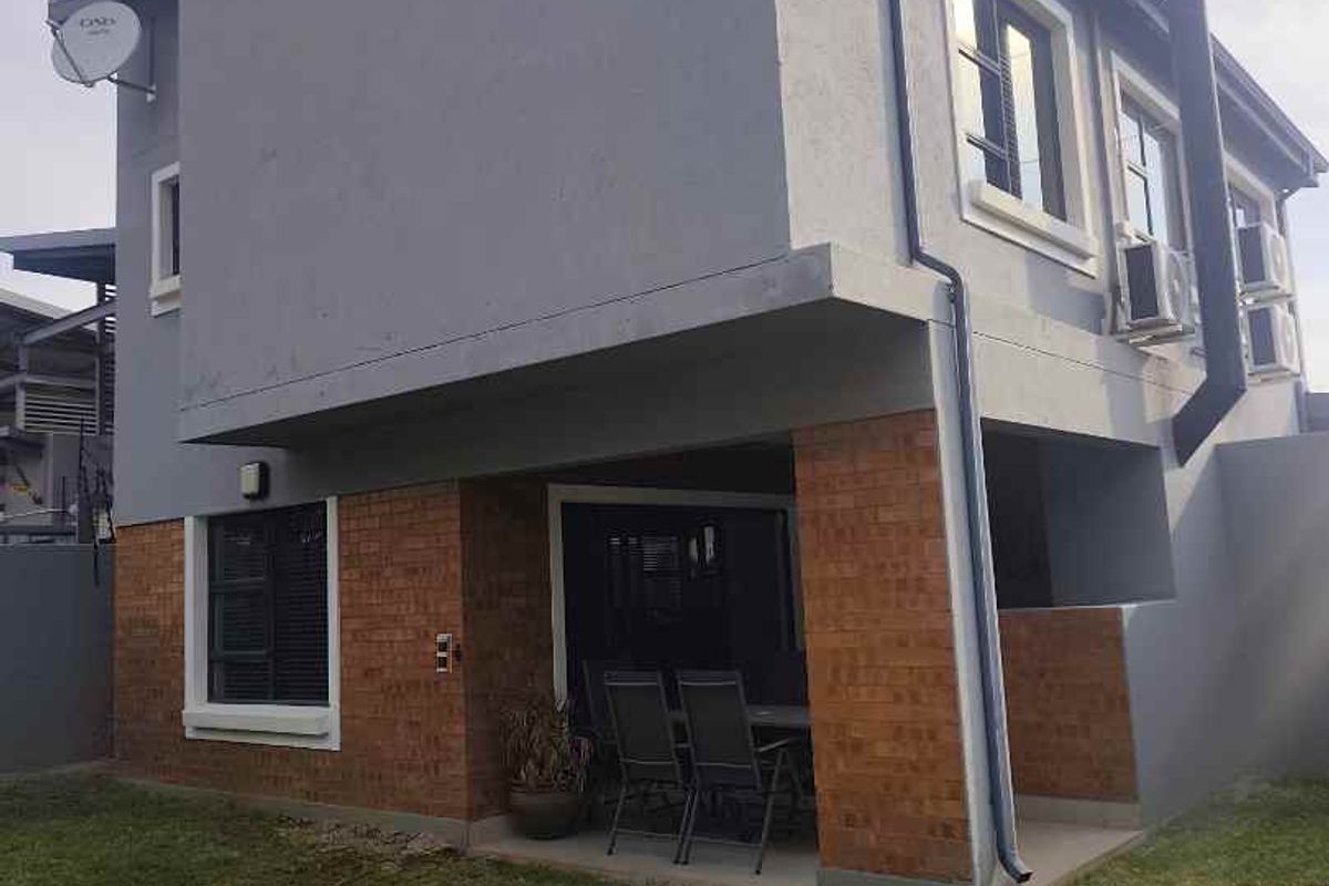 Rear view of a two-story house featuring a covered patio, brick and plaster exterior finishes, and external air conditioning units.