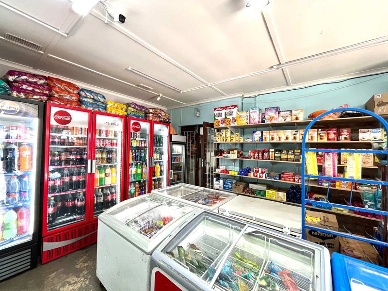A functional retail utility space featuring multiple commercial refrigeration units, chest freezers, and extensive fixed wall shelving for inventory storage.
