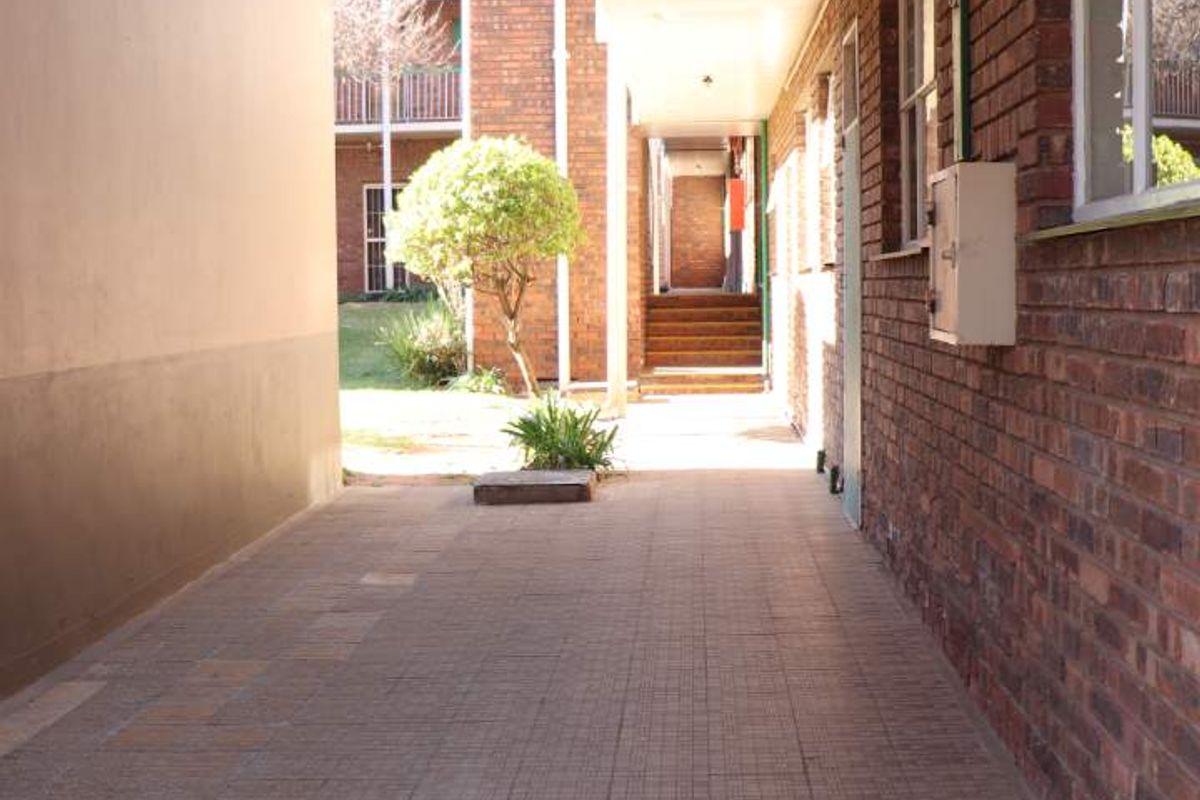 A covered exterior walkway between apartment blocks featuring brick walls and paved flooring, providing access to the residential units.