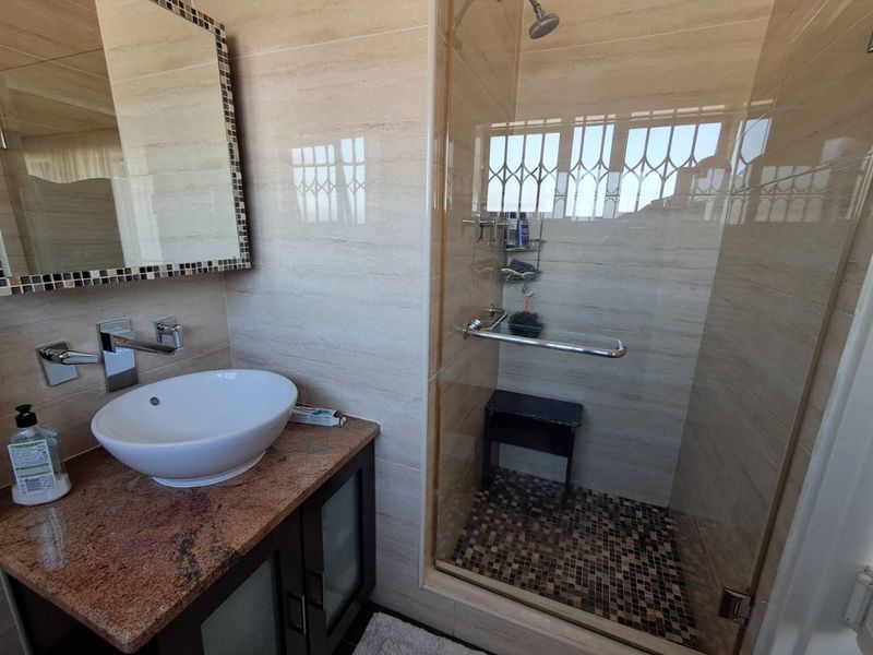 Modern bathroom featuring a vessel sink on a granite vanity, tiled walls, and a glass-enclosed shower with mosaic floor detailing.