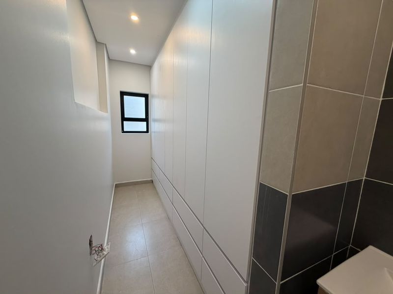 A modern, empty bedroom featuring extensive built-in white cabinetry, neutral tiled flooring, and recessed lighting, offering a clean and minimalist living space.