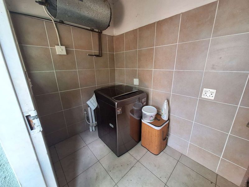 A functional laundry area featuring tiled walls and flooring, equipped with plumbing connections and an overhead electric water heater.