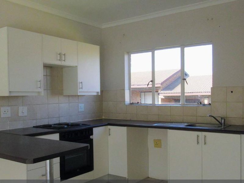 A functional kitchen featuring white cabinetry, dark laminate countertops, a built-in oven and hob, and a tiled backsplash with a window view.