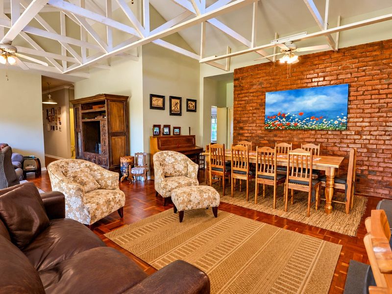 Spacious open-plan living and dining area featuring high vaulted ceilings with exposed timber trusses, a striking brick feature wall, and classic parquet flooring.