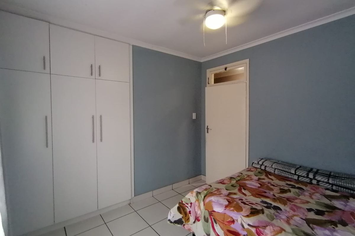 A functional bedroom featuring built-in cupboards, tiled flooring, and a ceiling fan, offering a clean and simple living space.
