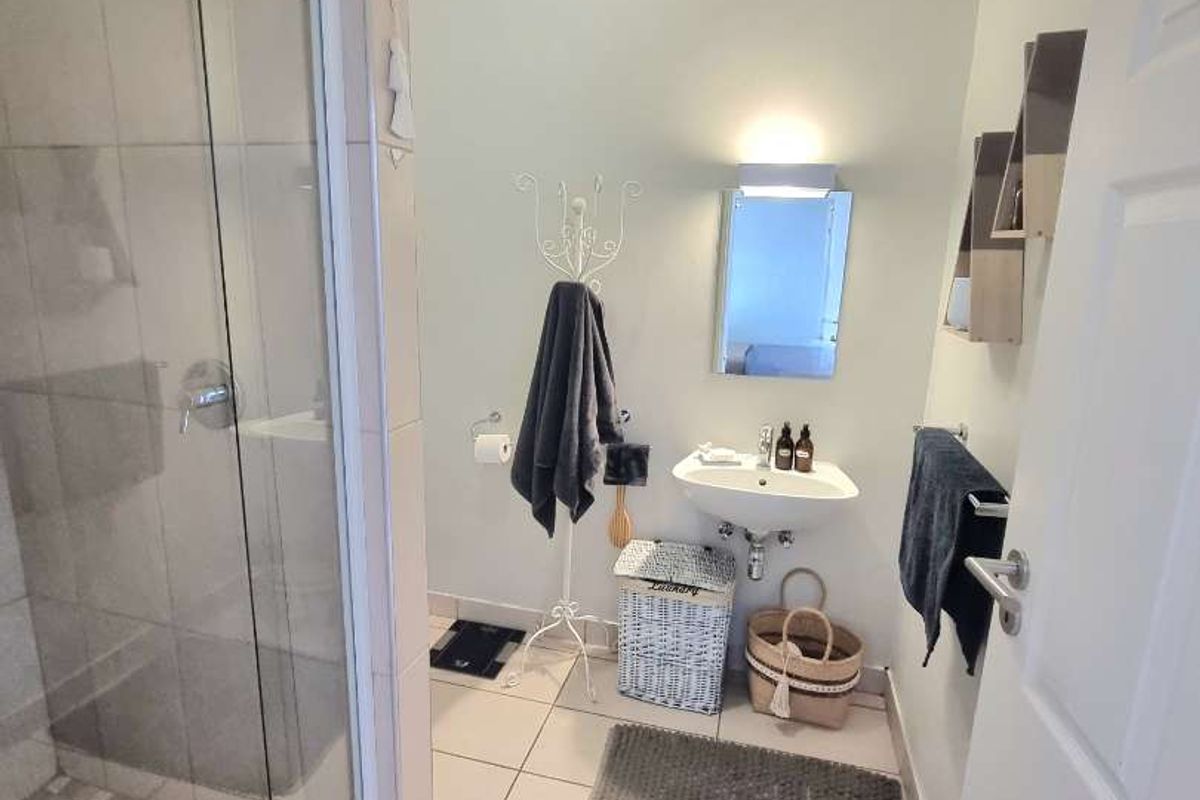 A clean and functional bathroom featuring a glass-enclosed shower, wall-mounted basin, and neutral tiled flooring.
