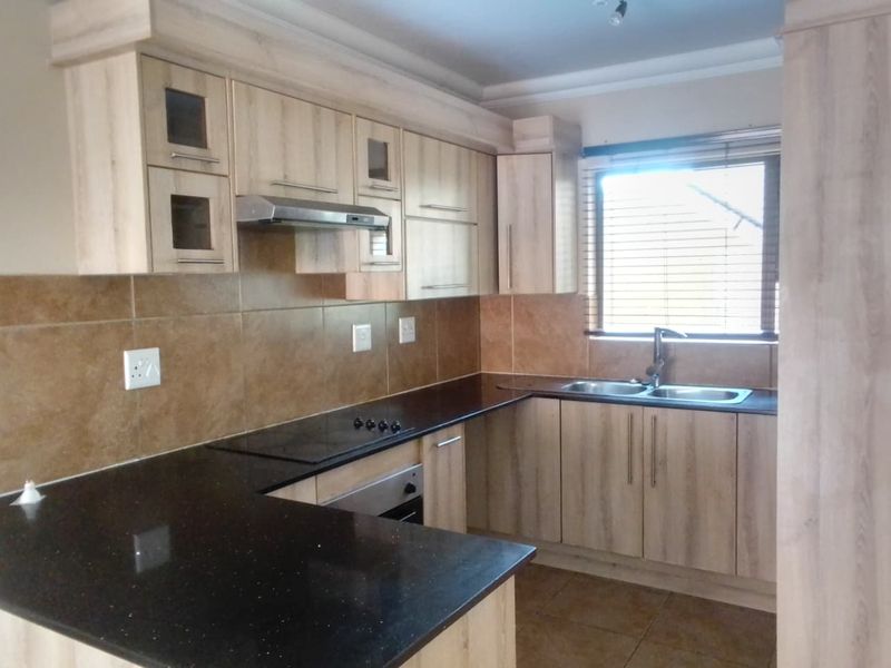A functional kitchen featuring light wood-look cabinetry, dark granite countertops, a double basin sink, and built-in cooking appliances with a tiled backsplash.
