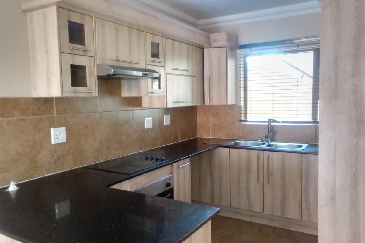 A functional kitchen featuring light wood-look cabinetry, dark granite countertops, a double basin sink, and built-in cooking appliances with a tiled backsplash.