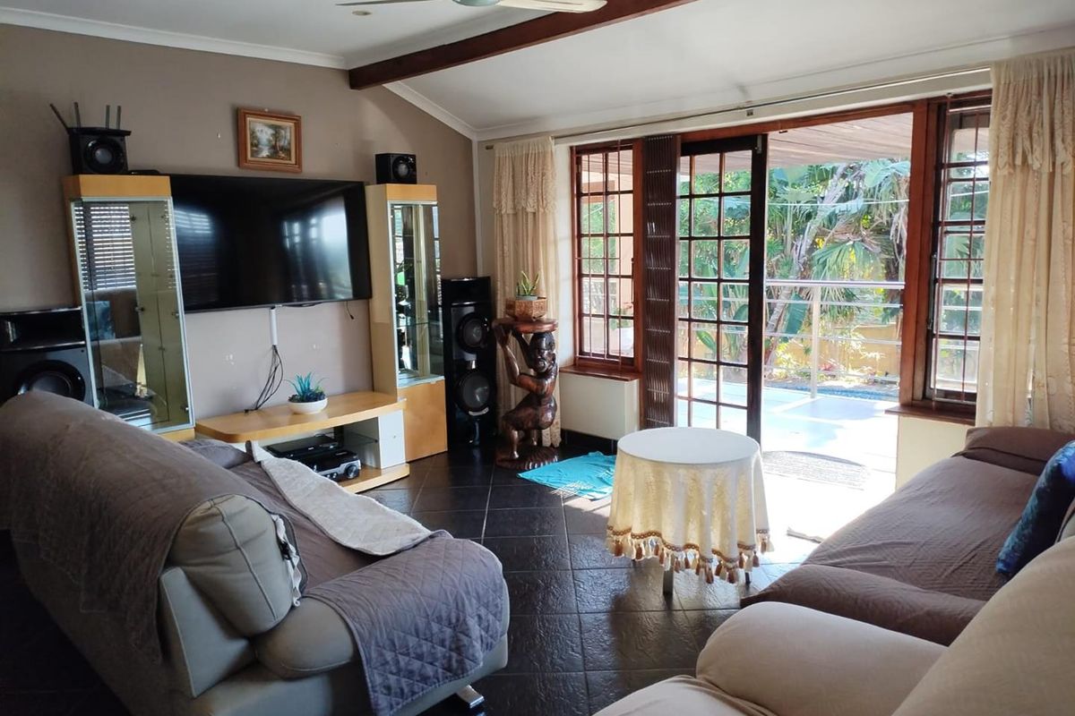 Spacious living room featuring dark tiled flooring, a ceiling fan, and large wooden-framed glass doors providing direct access to the outdoor patio area.