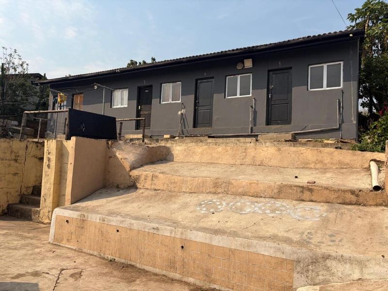 Rear view of a multi-unit residential building featuring dark painted exterior walls, aluminium windows, and tiered concrete steps showing signs of wear.