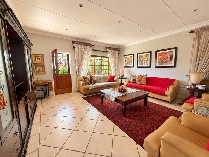 Spacious living room featuring neutral walls, tiled flooring, and natural light through a timber-framed window and door with security gate.