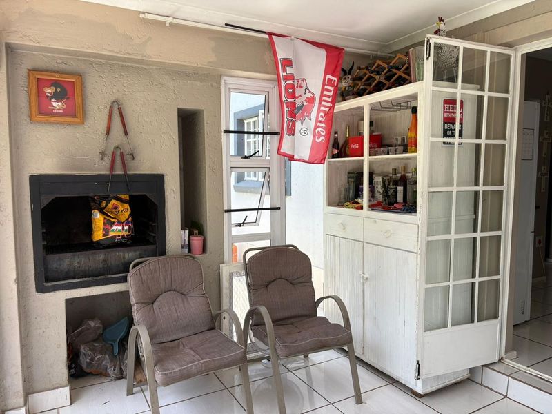 Covered patio area featuring a built-in braai, tiled flooring, and aluminium window frames, offering a functional outdoor entertainment space.
