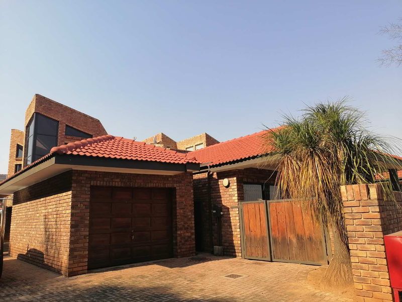 Front elevation of a face brick house featuring a tiled roof, paved driveway, wooden garage door, and a private pedestrian entrance gate.