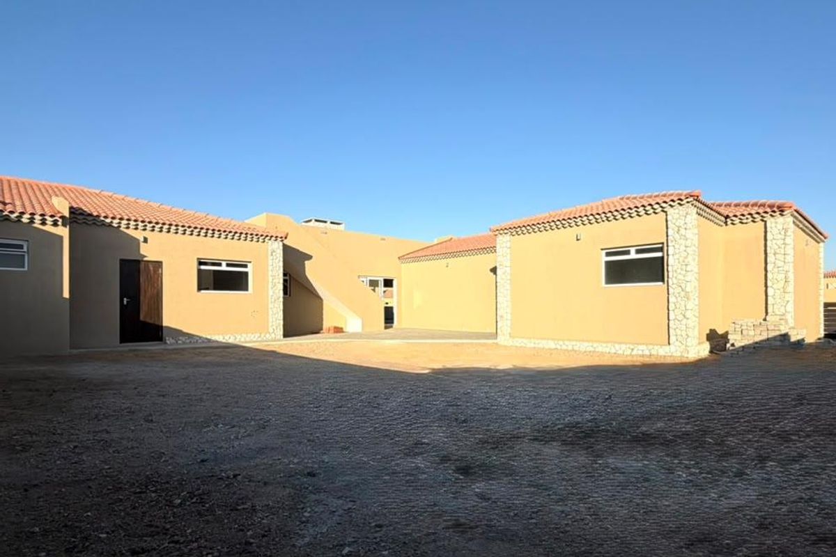 Rear view of the property featuring a stucco facade with stone accents, terracotta roof tiles, and an expansive unpaved courtyard area.