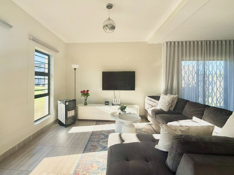A bright and well-maintained living room featuring tiled flooring, a recessed ceiling, and large windows with access to an outdoor area via a sliding door.