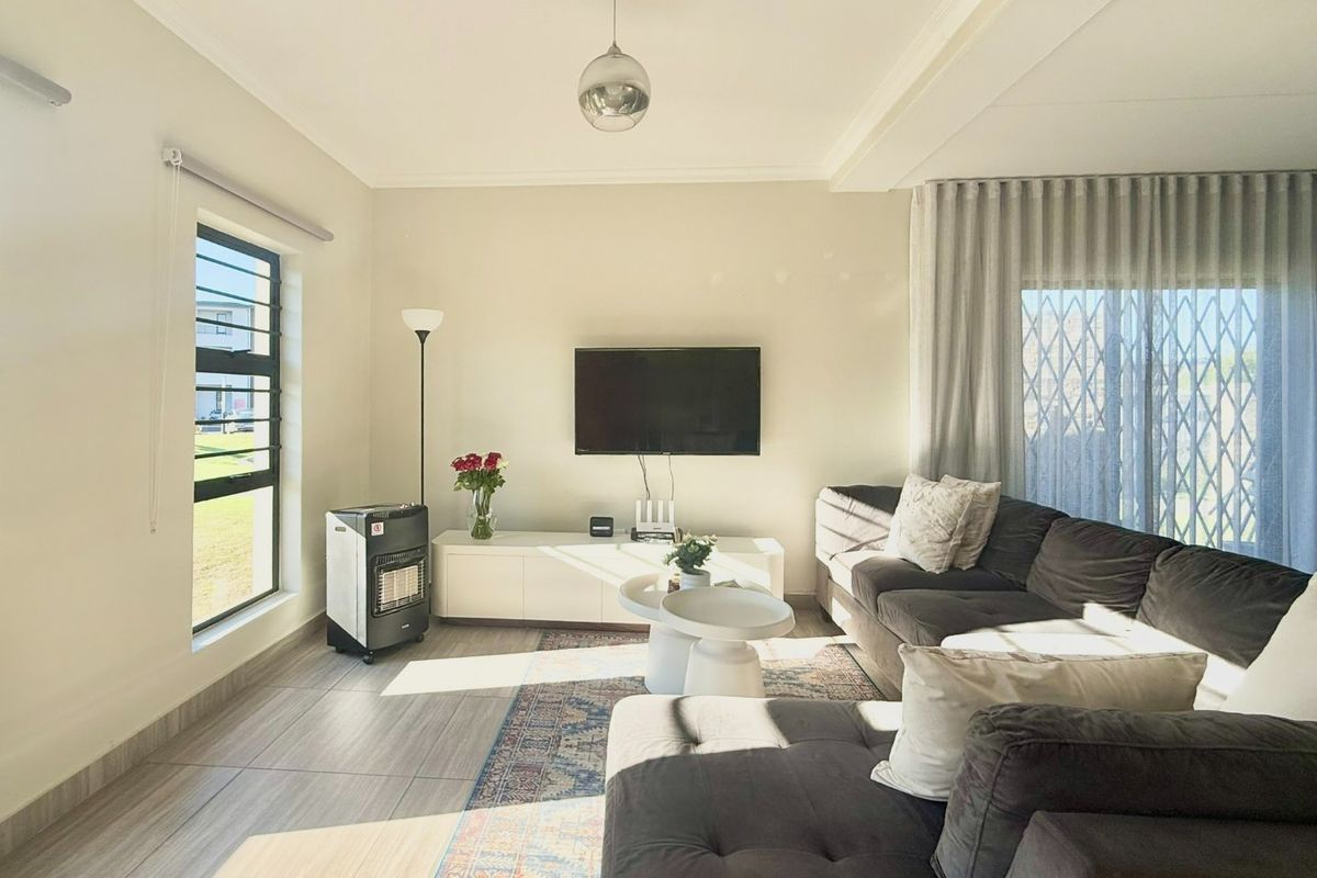 A bright and well-maintained living room featuring tiled flooring, a recessed ceiling, and large windows with access to an outdoor area via a sliding door.