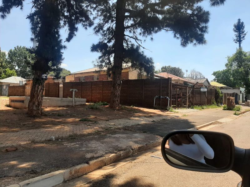 Street view of the property showing the boundary wall, security fencing, and paved verge area from the roadside.