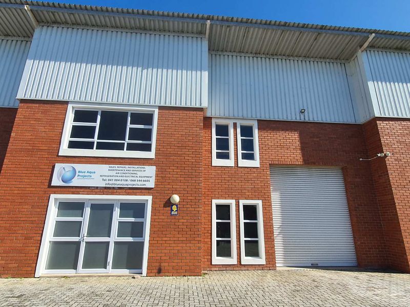 Front elevation of a commercial industrial unit featuring brickwork, corrugated metal cladding, roller shutter access, and aluminium-framed windows.